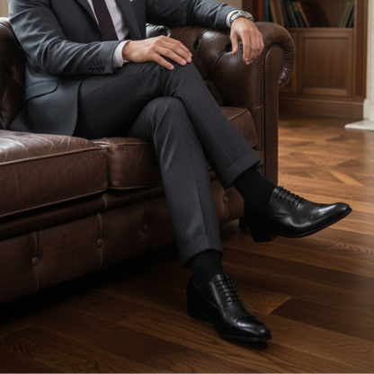 Man in a suit sitting on a brown leather sofa in a room with bookshelves and a fireplace.